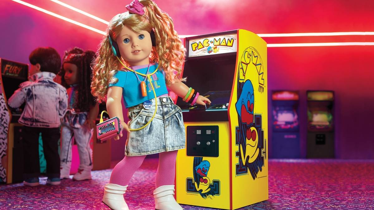 American Girl doll Courtney Moore stands next to a Pac-Man arcade cabinet.