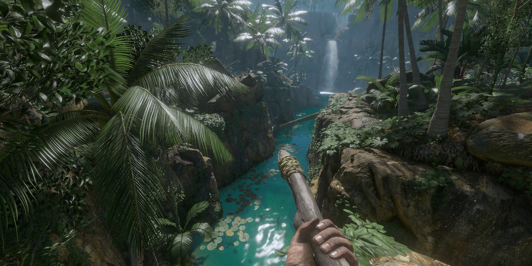 A player holding a spear looking at a waterfall in Green Hell