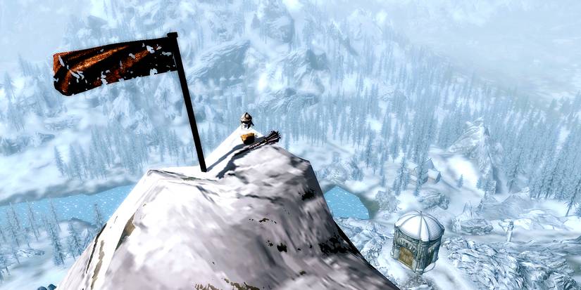 peak of a snowy mountain with a flag and some items overlooking skyrim