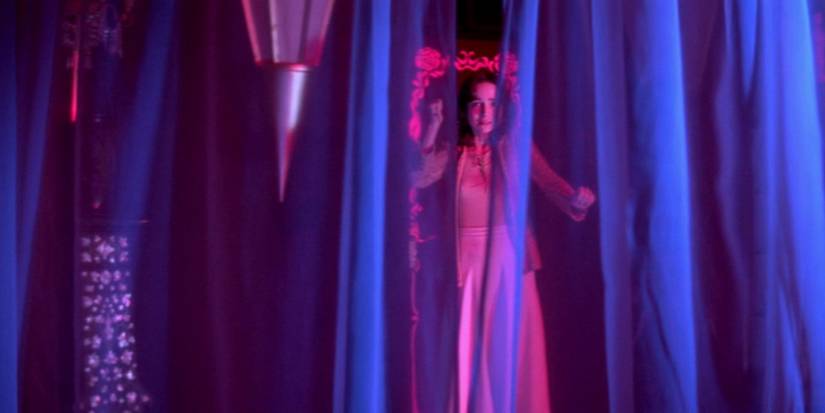 Suspiria Film Still girl behind blue curtains, scared, holding a knife in pink lighting