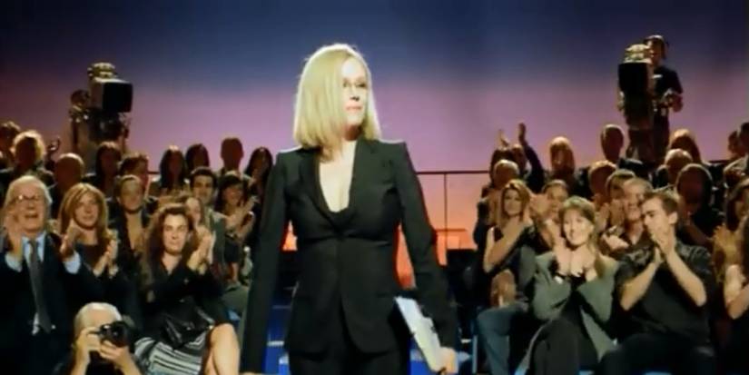 The Vanity Serum still of blonde women in suit between TV audience with camera crew behind her