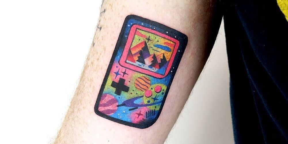 Colorful gameboy tattoo with space and mountain themes.