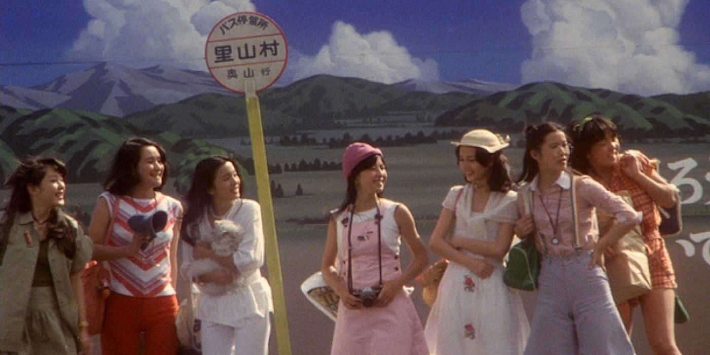 The seven girls wait at a bus stop against a beautiful landscape in Hausu