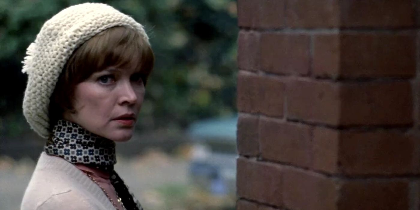 Ellen Burtsyn standing outside in warm clothing, facing a brick wall in a scene from The Exorcist