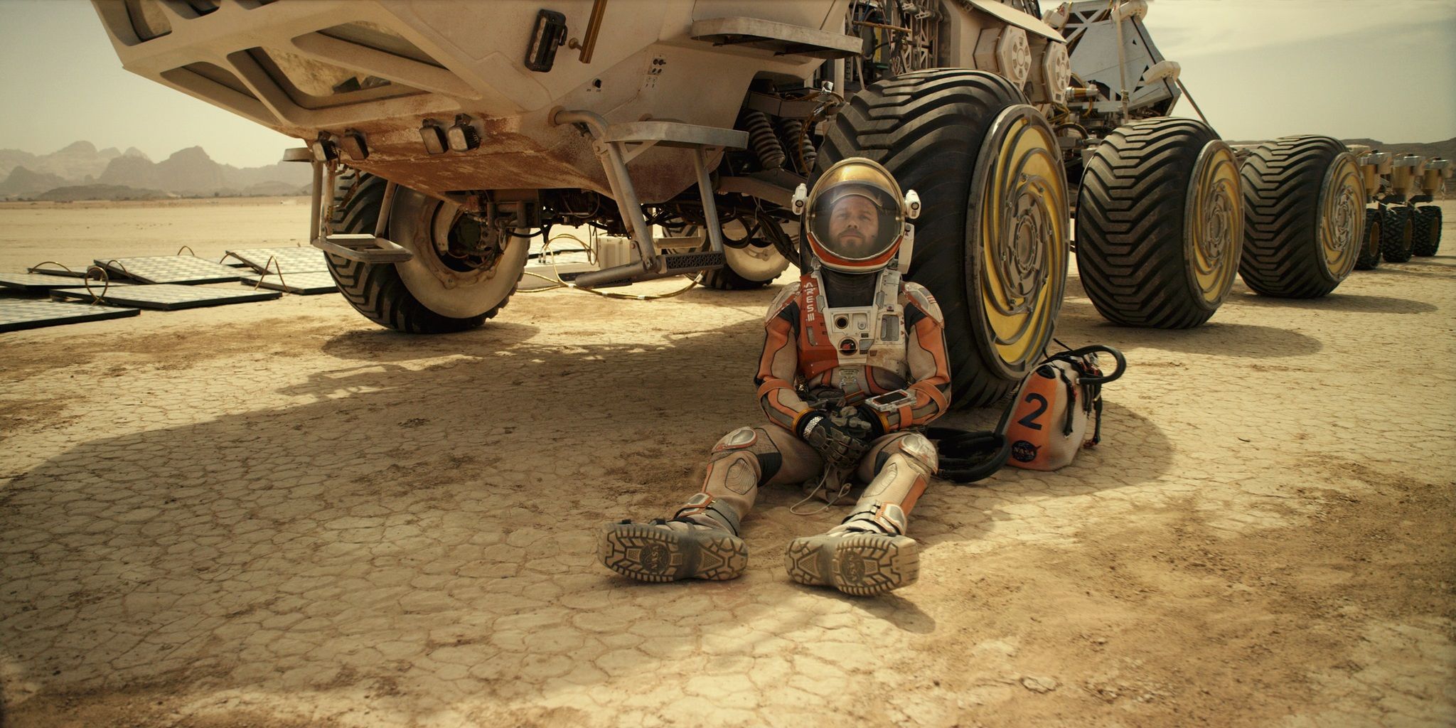 Мэтт Дэймон в роли Марка Уотни сидит напротив марсохода на Марсе в фильме «Марсианин».