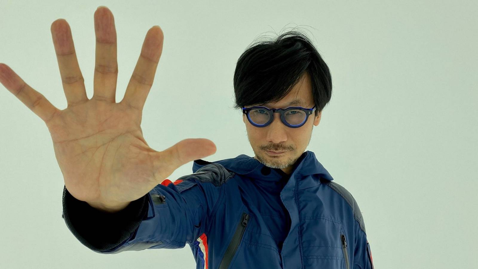 A photo of Hideo Kojima with his open hand up to the camera.