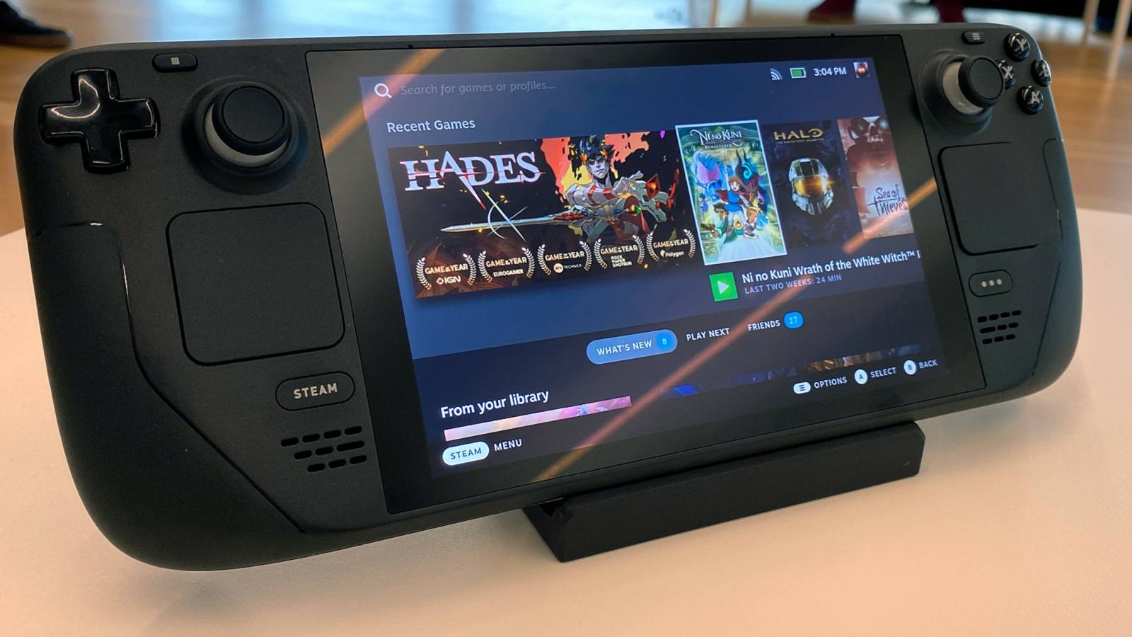 A photo of a Steam Deck on a stand, with the screen showing a list of recent games played.