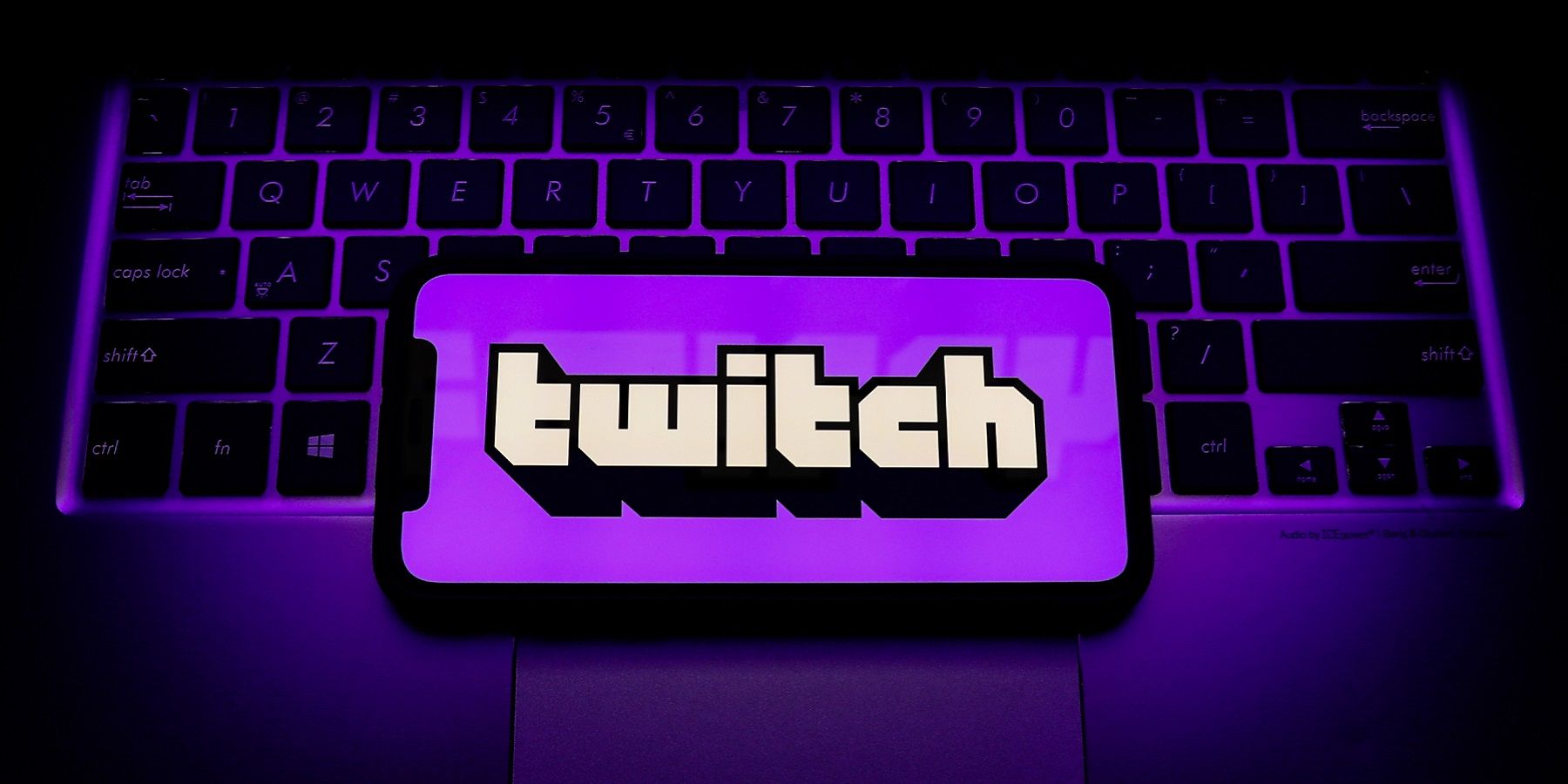 Purple tinted image showing a laptop keyboard and a phone screen over it with the Twitch logo.