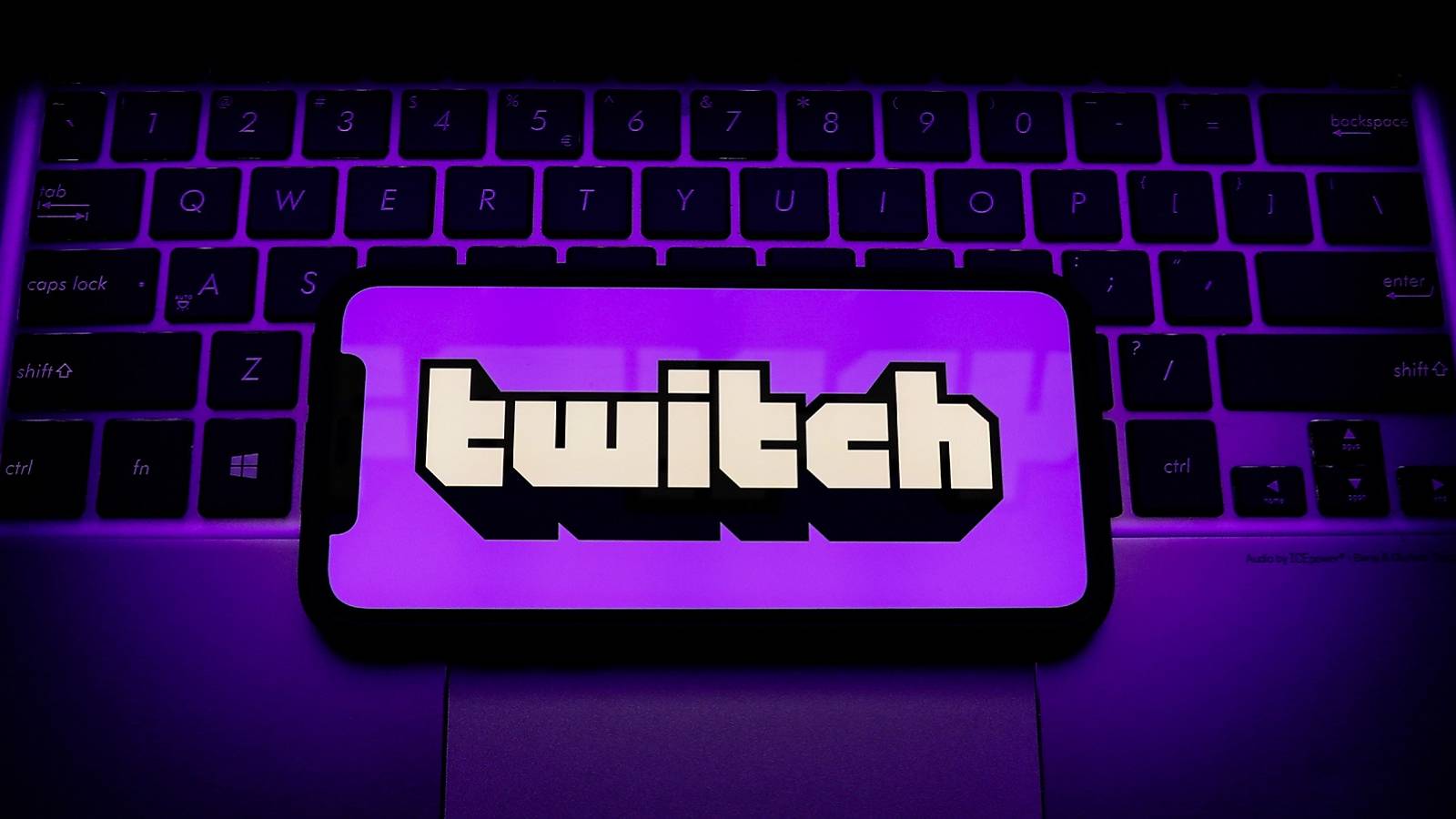 Purple tinted image showing a laptop keyboard and a phone screen over it with the Twitch logo.