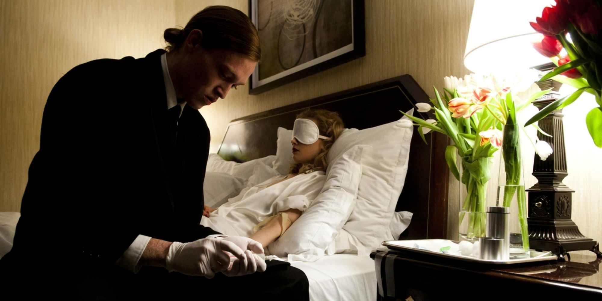 A man fills a syringe while a woman with a sleep-mask lies in bed in Antiviral
