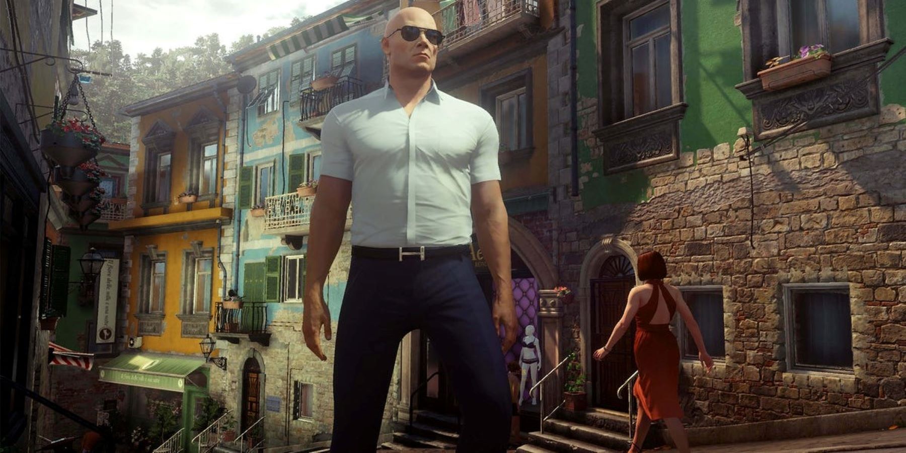 Агент 47 в темных очках стоит на улице в Сапиенце, Италия, во время миссии «Мир завтрашнего дня» в Hitman: Game of the Year Edition.