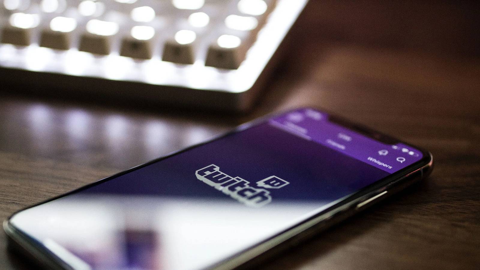 A photograph of a smartphone on a table, with the screen showing the Twitch logo.