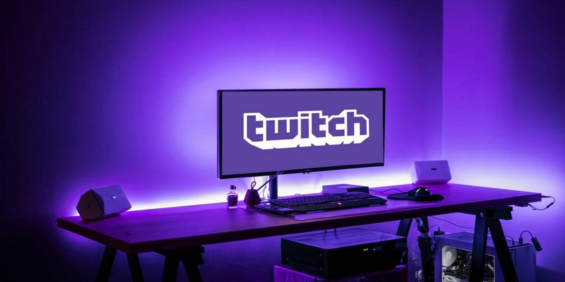 A phot of a PC monitor on a desk showing the Twitch logo, all glowing purple.