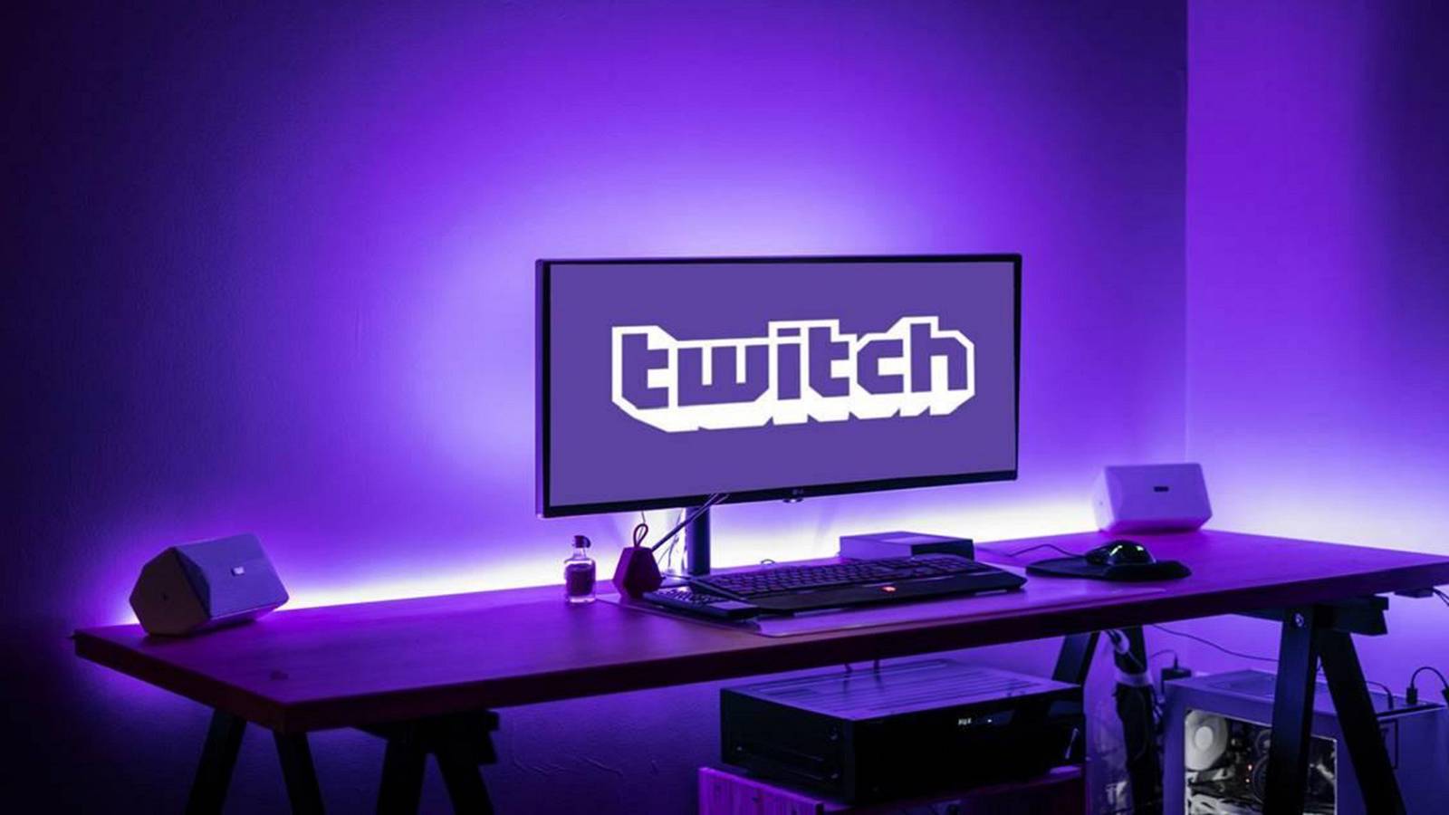 A phot of a PC monitor on a desk showing the Twitch logo, all glowing purple.