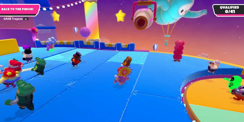 a fall guy bean stands in the middle of a blue platform facing a large, mounted cannon