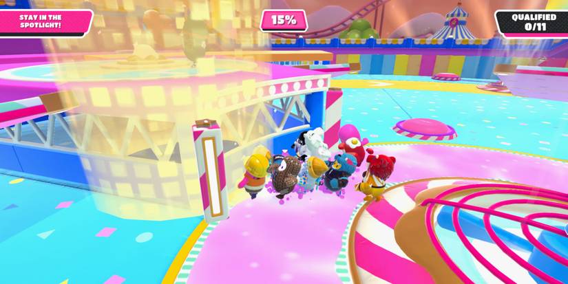 a cluster of fall guy beans standing at the bottom of a wall trying to get to a golden spotlight 