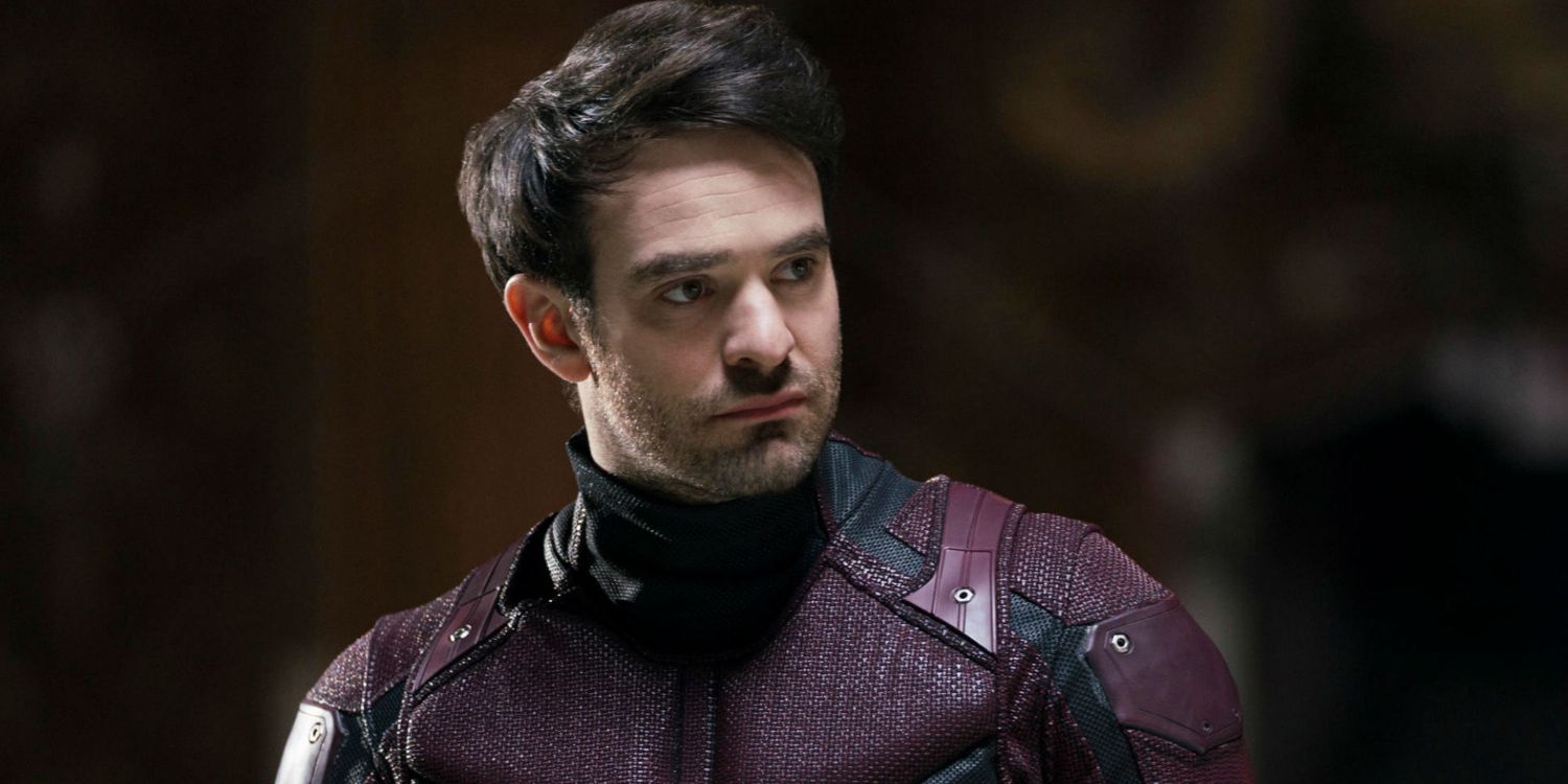 charlie cox as daredevil in his red suit but without a mask, looks to one side with a frown