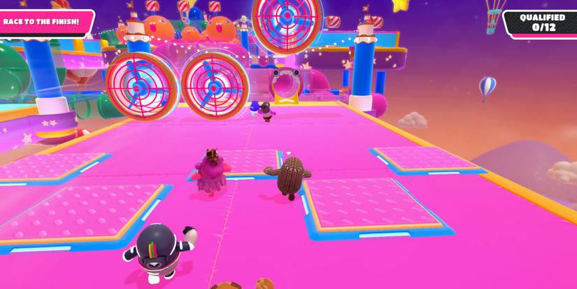 a group of fall guy beans running across a pink platform toward a row of fans blowing at them