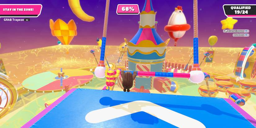 two fall guy beans swinging from a trapeze bar over a large, yellow boxed obstacle course 