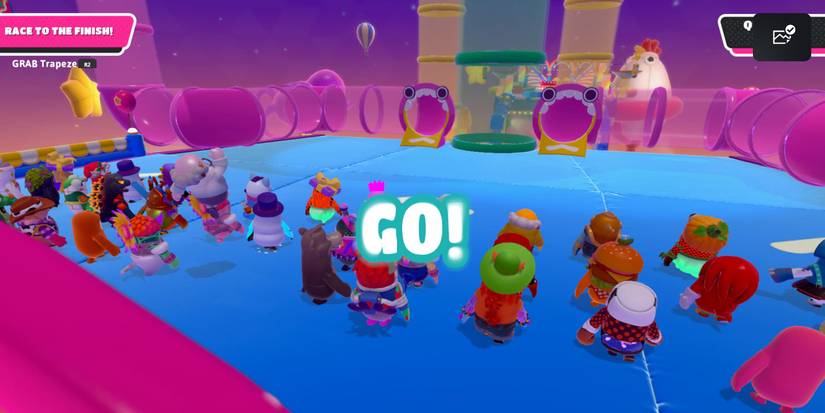 a group of fall guy beans at the start of a round with two pipe entrances shaped like mouths in front of them