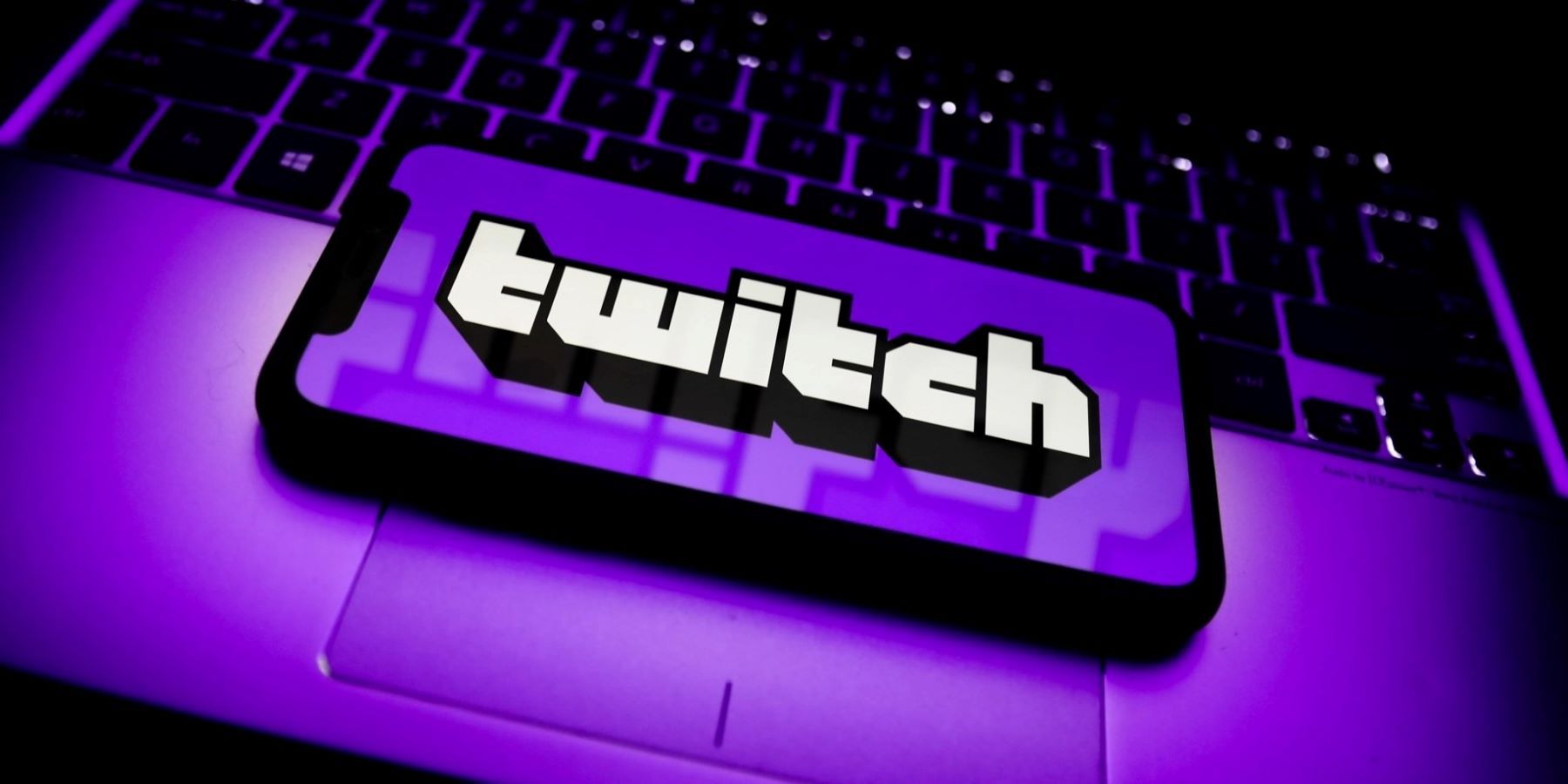 A purple cellphone with Twitch's name on its screen resting on the trackpad of a laptop