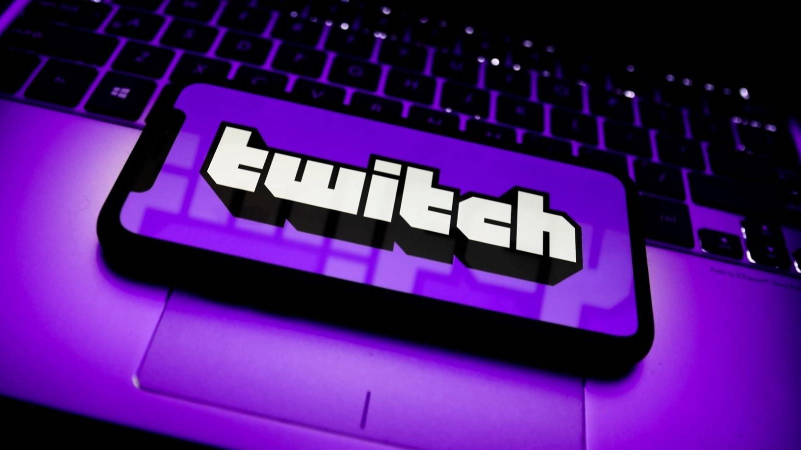 A purple cellphone with Twitch's name on its screen resting on the trackpad of a laptop