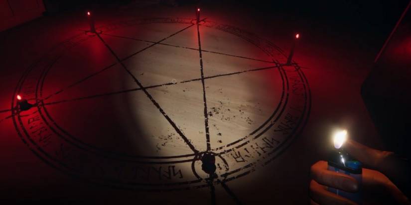 Screenshot from Phasmophobia showing a pentagram on the ground with red candles around it.