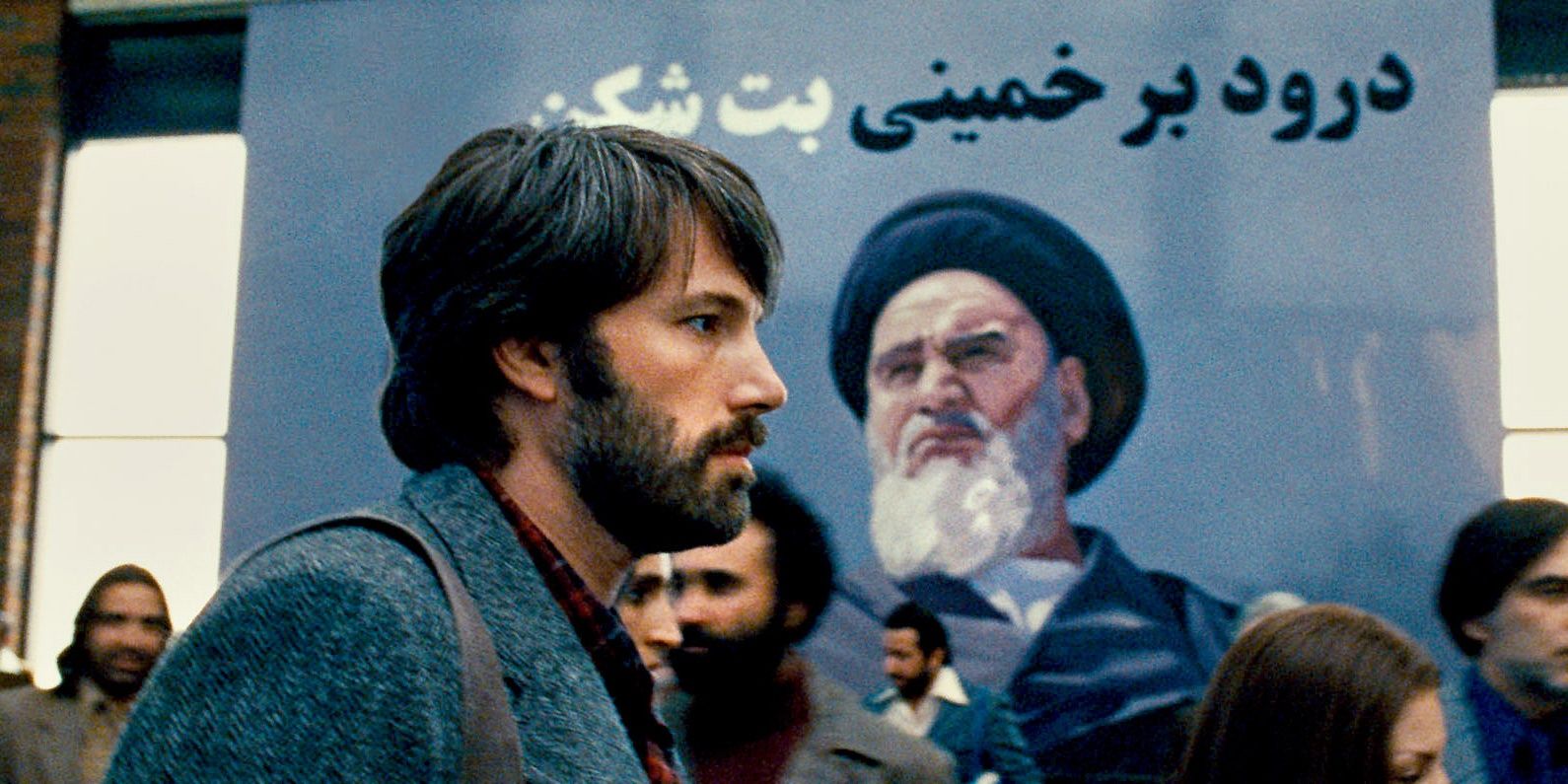 Бен Аффлек в роли Тони Мендеса проходит мимо плаката с изображением Ирана