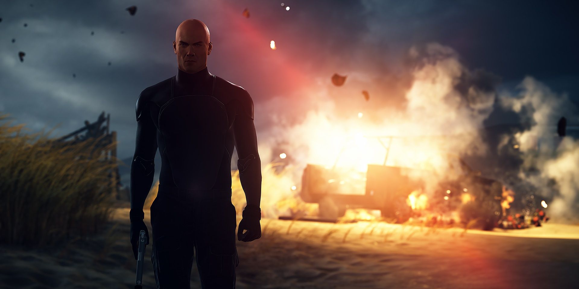 Agent 47 walks away from an explosion on the beach of Hawke's Bay in Hitman 2