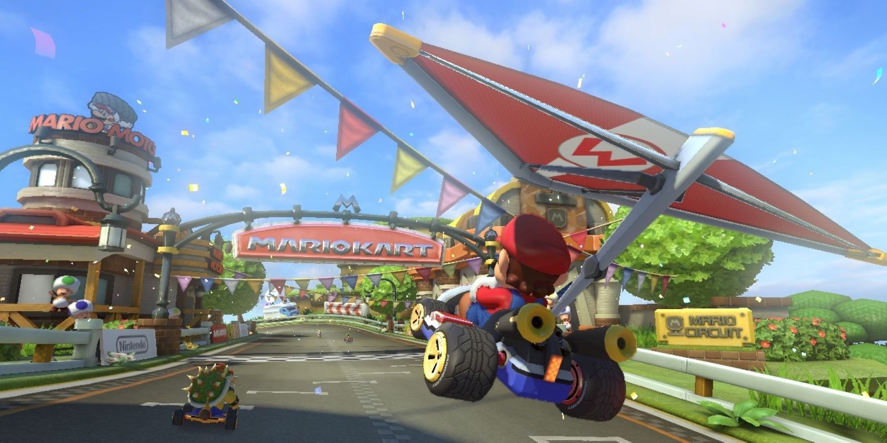 Mario gliding toward the finish line of a Mario Kart course with Bowser and a couple Toads in view