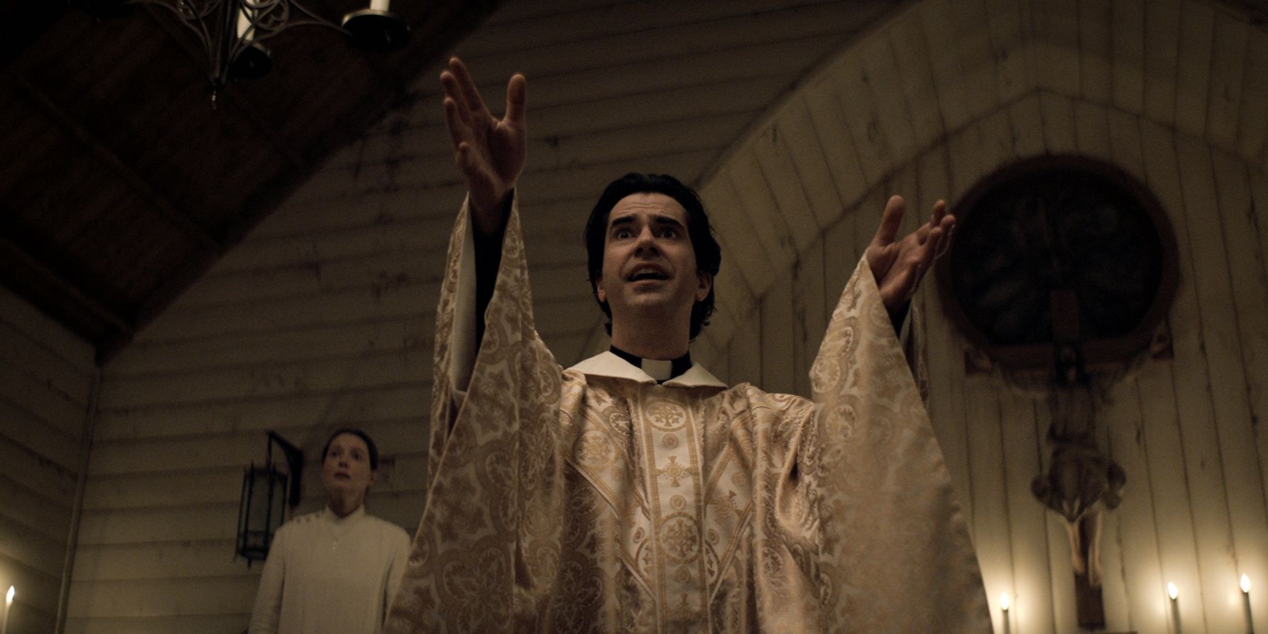 Отец Пол поднимает руки во время службы при свечах в шоу Netflix Midnight Mass.