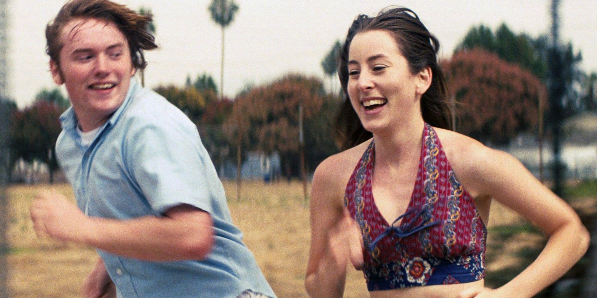 Alana Haim and Cooper Hoffman running alongside each other in Licorice Pizza