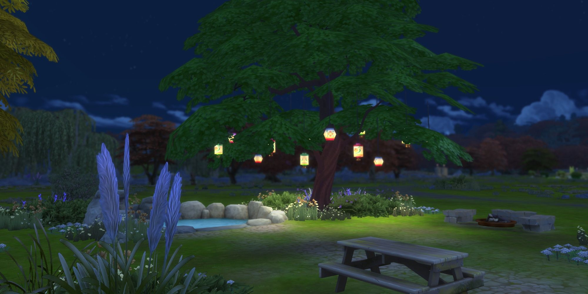 A quiet picnic area in the Sims 4 with a large oak tree holding numerous paper lanterns at night.