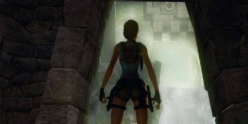 Lara Croft stands in a shadowed archway facing into an opening in the distance