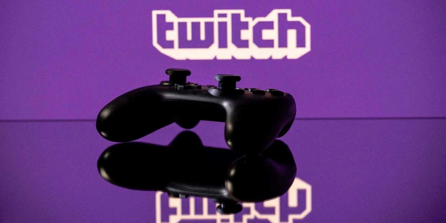 A Nintendo Switch Pro Controller on a reflective surface in front of the Twitch logo