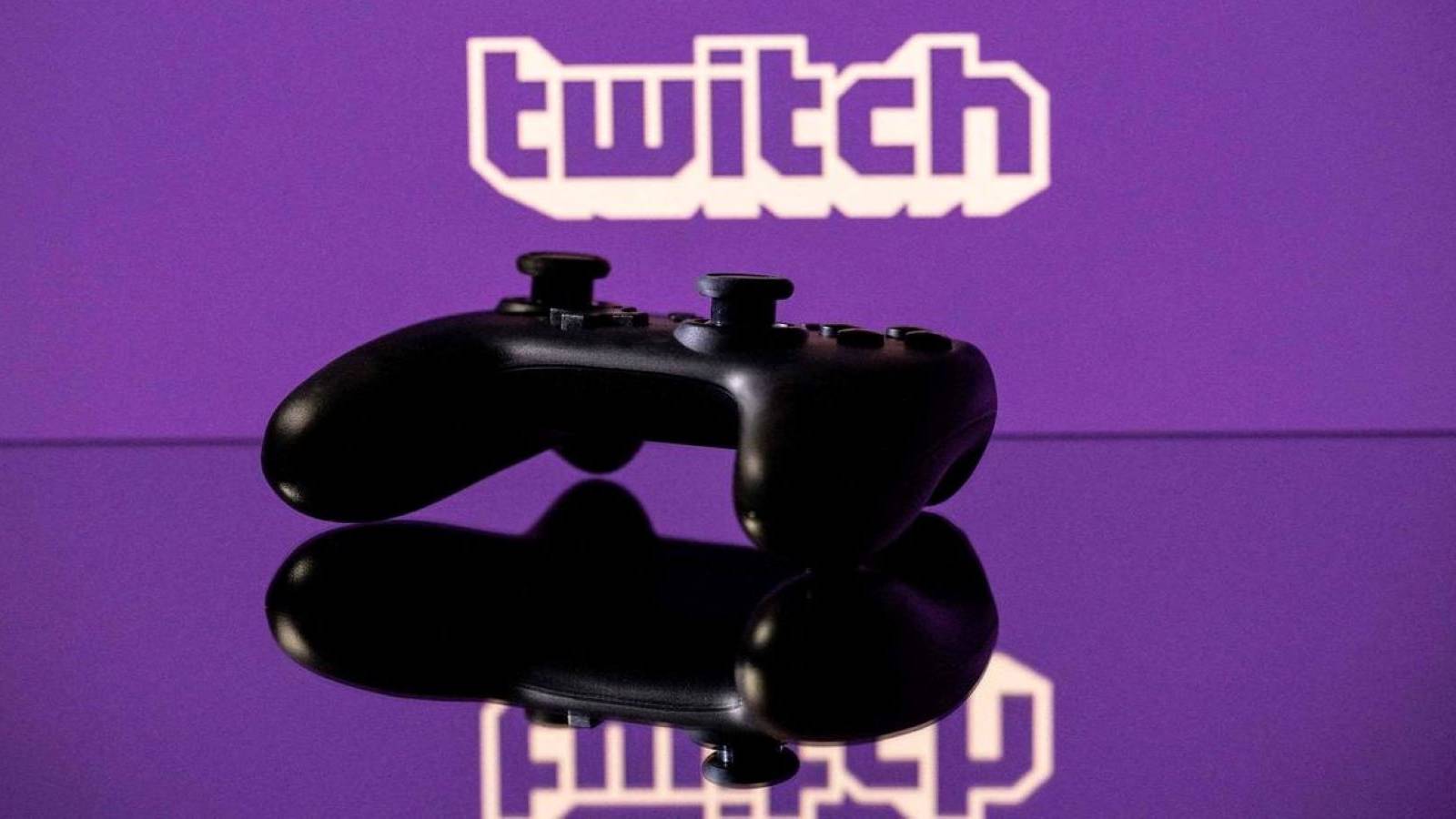 A Nintendo Switch Pro Controller on a reflective surface in front of the Twitch logo