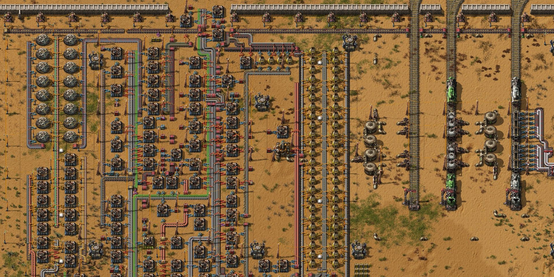 A series of assembly lines, refineries, and railroad tracks in the game Factorio