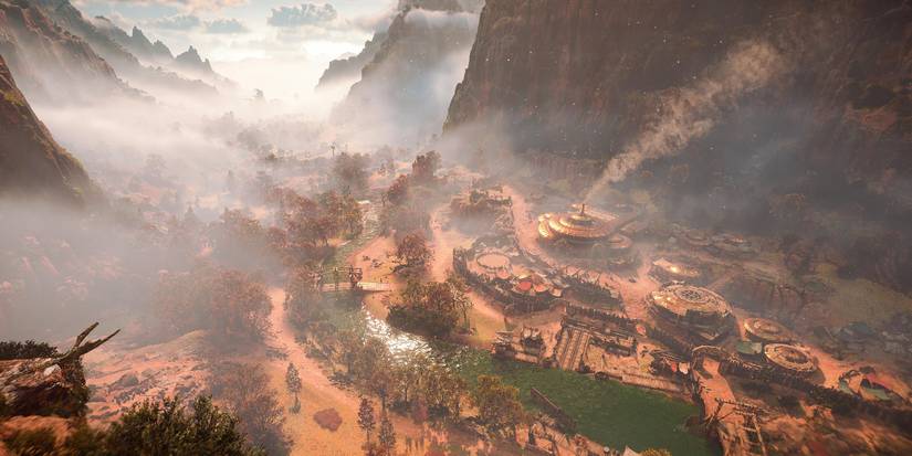 a landscape shot of a town with circular buildings in a valley with foggy mountains on either side 