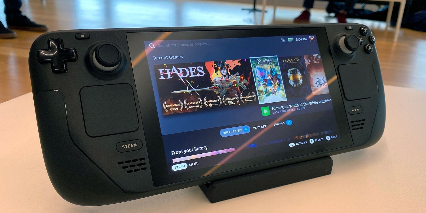A Steam Deck on a holder showing a recent games list on-screen.