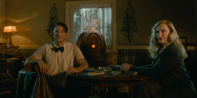 Stan (Bradley Cooper) and Zeena (Toni Collette) smile next to a table and old radio in Nightmare Alley