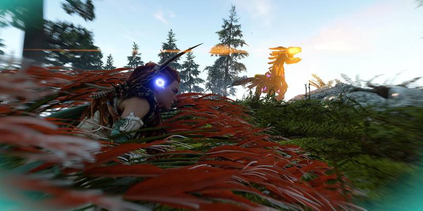 aloy hiding in tall, red grass from a nearby robot raptor with glowing yellow eyes
