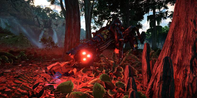 A lithe machine with black armor and glowing red eyes standing between some trees with a waterfall in the distance