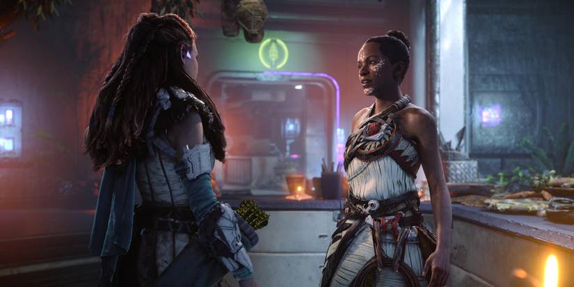 Zo and Aloy talking inside a metal bunker with scrolls and leatherbound books on the counter 