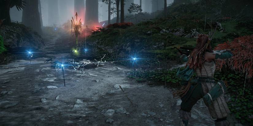 aloy standing on a dirt path in front of a set of electric wires attached to glowing blue posts and a green canister on a stick 