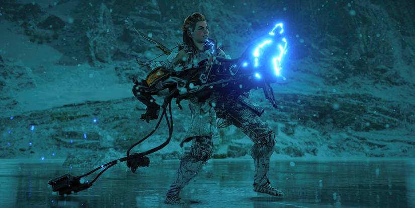 Aloy standing on a frozen lake with a large cannon in her hands that is sparking with blue electricity at its front end