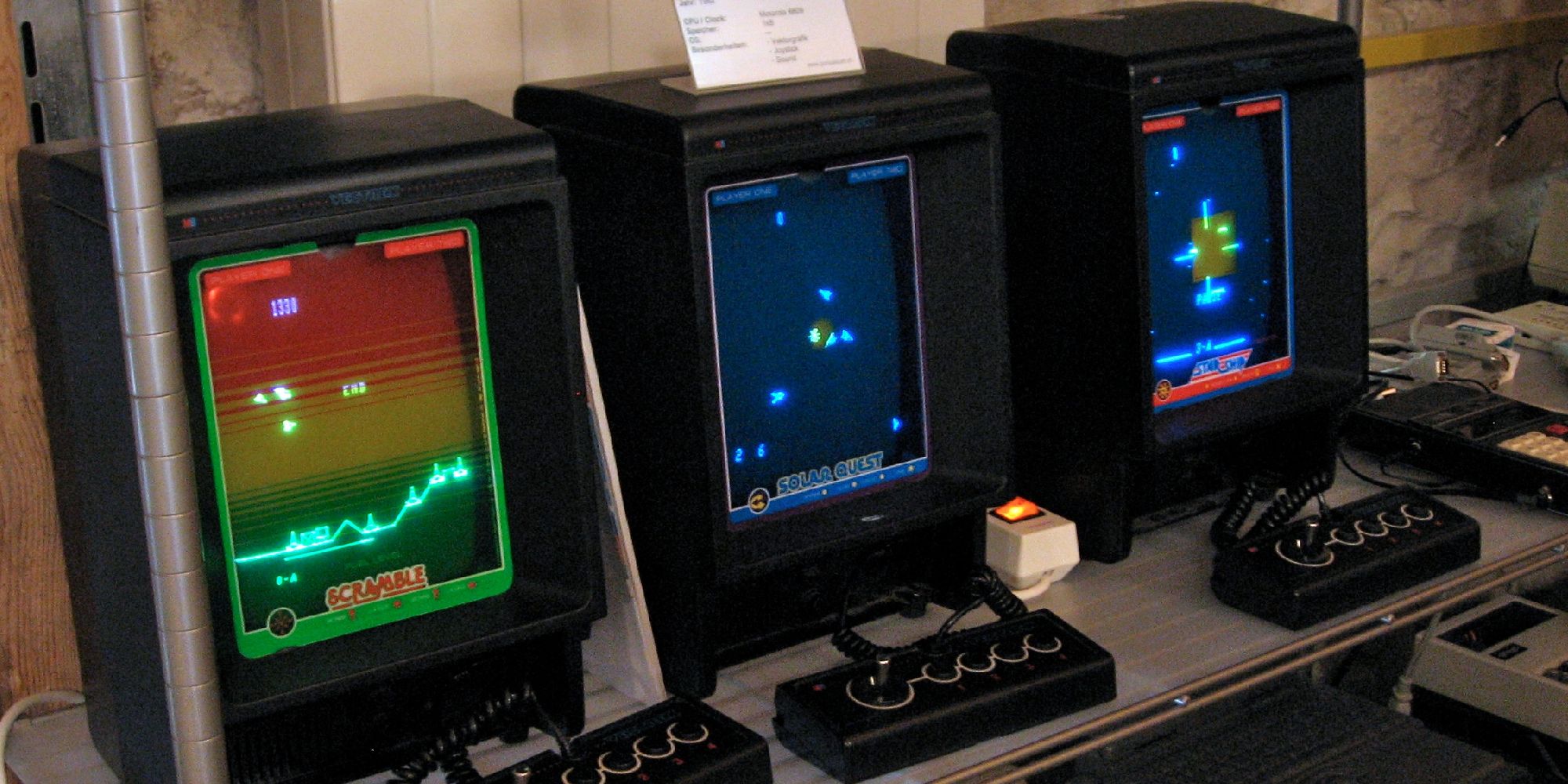 A row of three Vectrex consoles with controllers playing different games