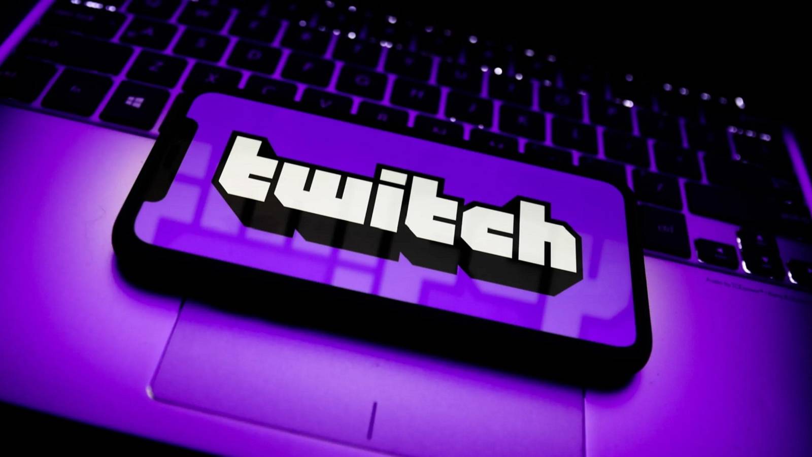 A phone on a laptop, with the Twitch logo and a purple background on the phone's screen.