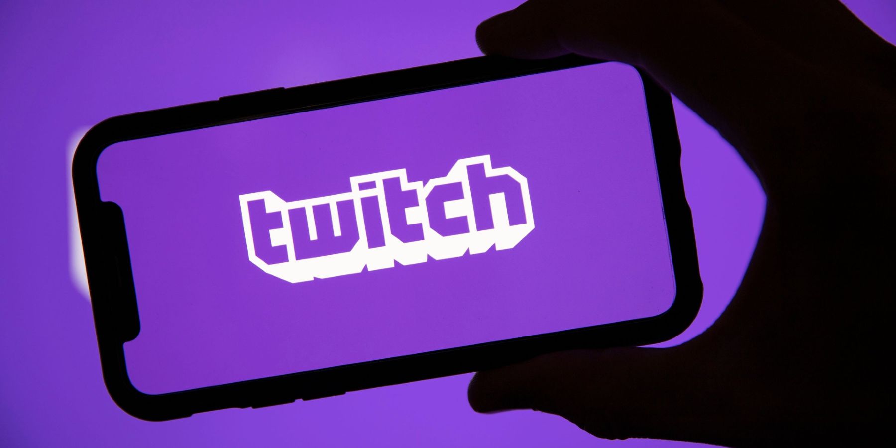 A phone being held up which shows the Twitch logo on the screen, all on a purple background.