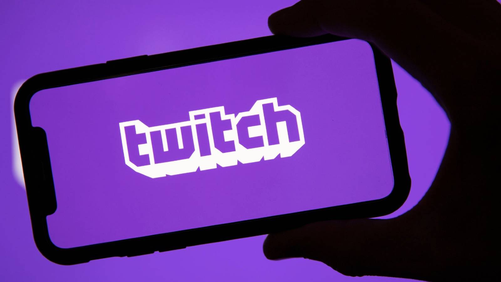 A phone being held up which shows the Twitch logo on the screen, all on a purple background.
