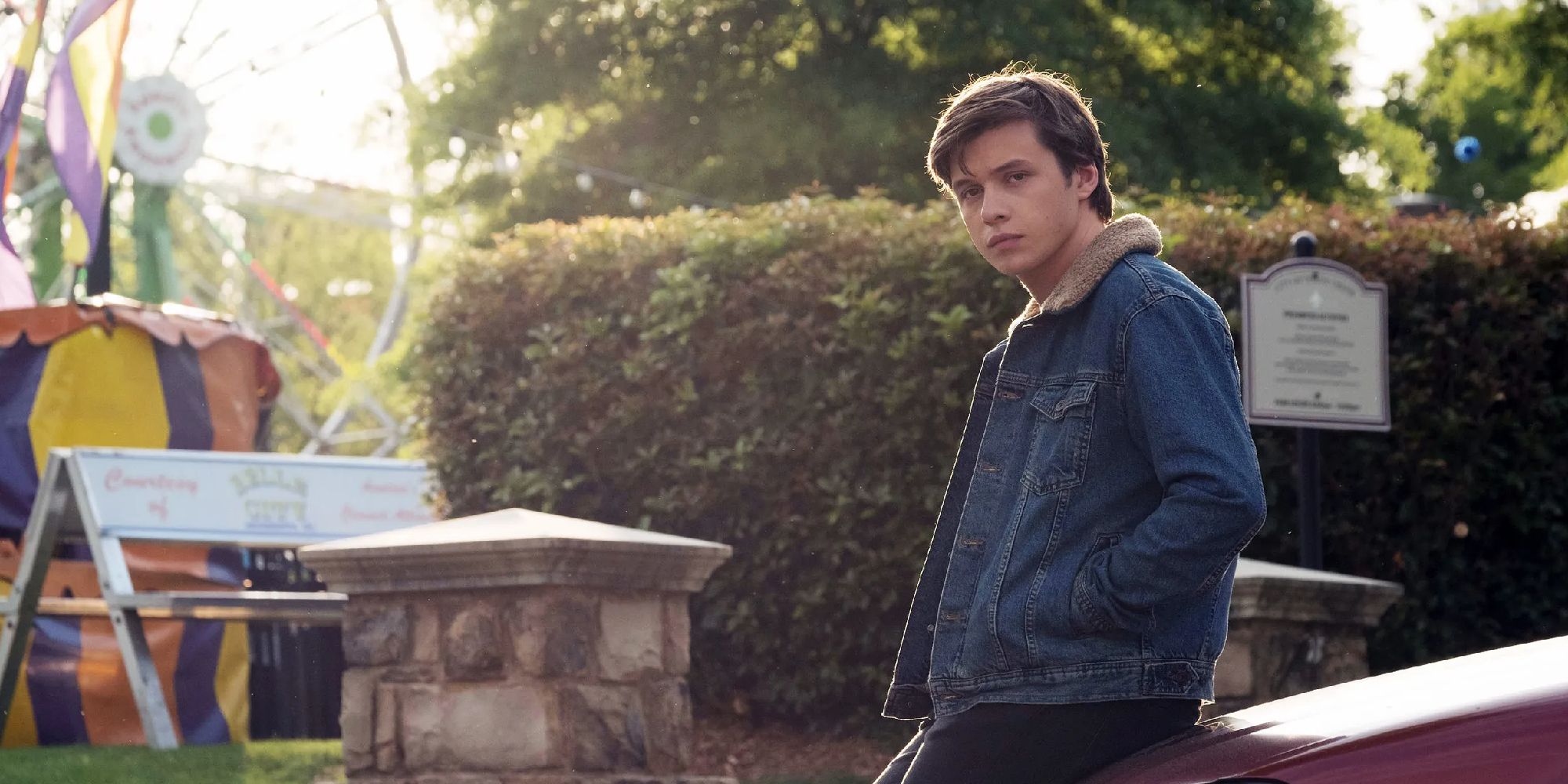 Nick Robinson as Simon leaning against a car near a state fair in Love, Simon